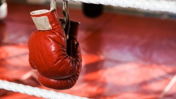 Close up of boxing gloves on the ropes of a boxing ring.